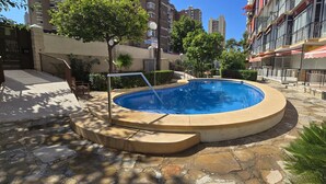 Piscina rodeada de baldosas de piedra, con una entrada protegida por una reja y una escalera que sube.