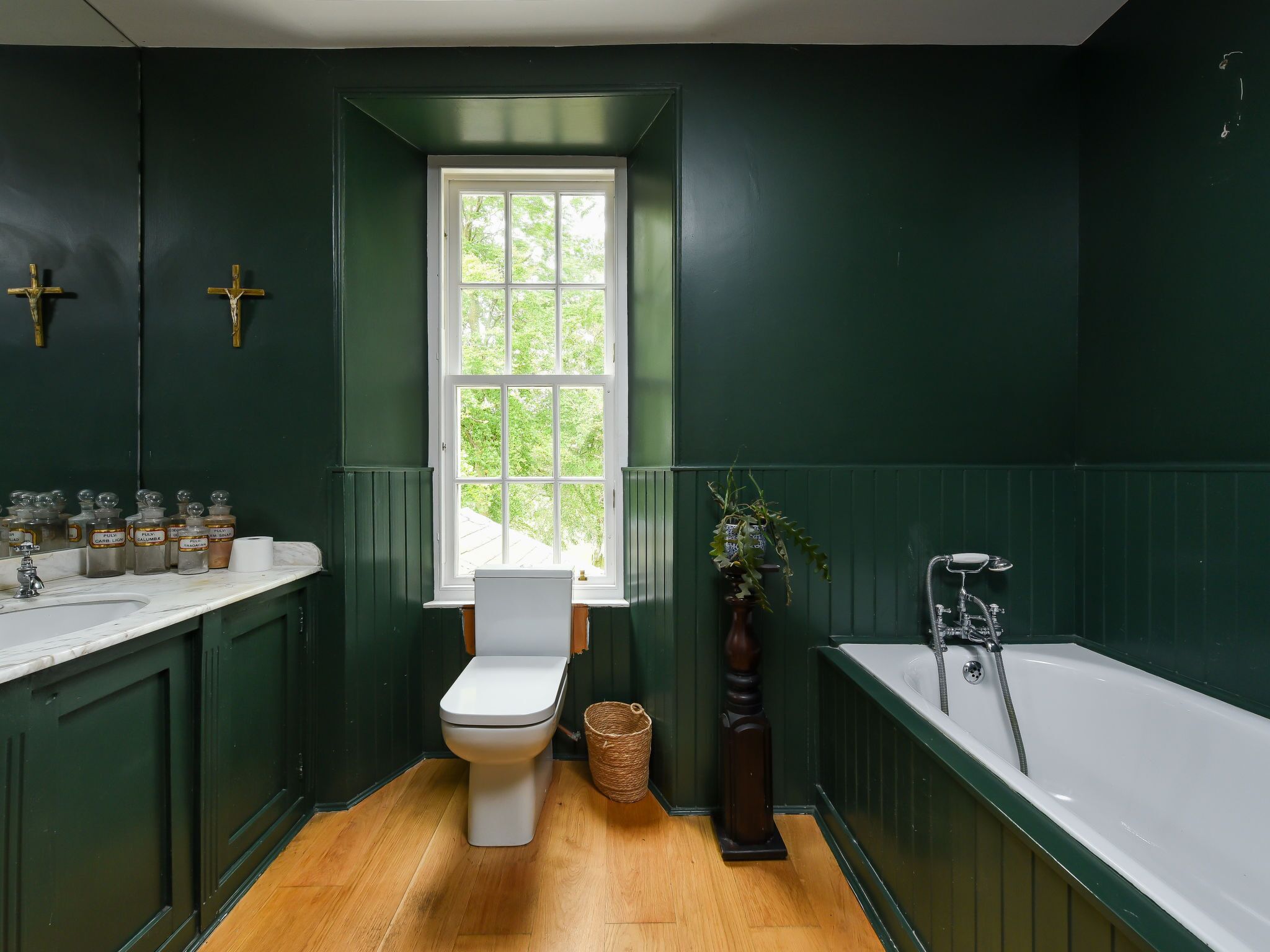 Een badkamer met een wit toilet, een raam, een badkuip en groene wanden.