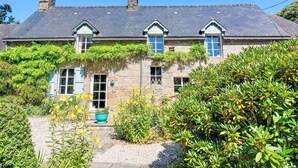 Ein Haus aus Stein mit einem geneigten Dach, von Efeu bewachsenen Mauern und einer Haustür mit blauem Türrahmen.