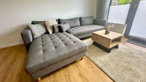 Una sala de estar moderna con un sofá seccional gris, una mesa de centro de madera y un ventanal con persianas.
