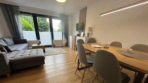 Una sala de estar moderna con un sofá, una mesa de comedor con sillas, un televisor y una ventana con cortinas.