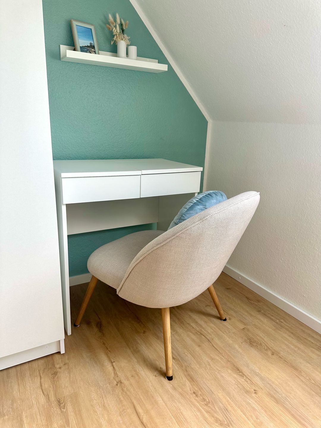 Ein Zimmer mit einem weißen Schreibtisch, einer Wand in Türkis und einem Stuhl mit blauer Sitzkissen.