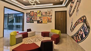 A modern lobby with a curved seating area, a film strip mural, and a glass wall offering a view of the outside. - Kratos Club (Surat)