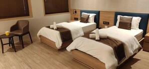 A hotel room with two beds, a small table, and a chair.