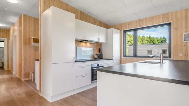 Eine moderne Küche mit weißen Schränken, einer Edelstahl-Spüle und einem großen Fenster mit Blick auf Grünflächen.