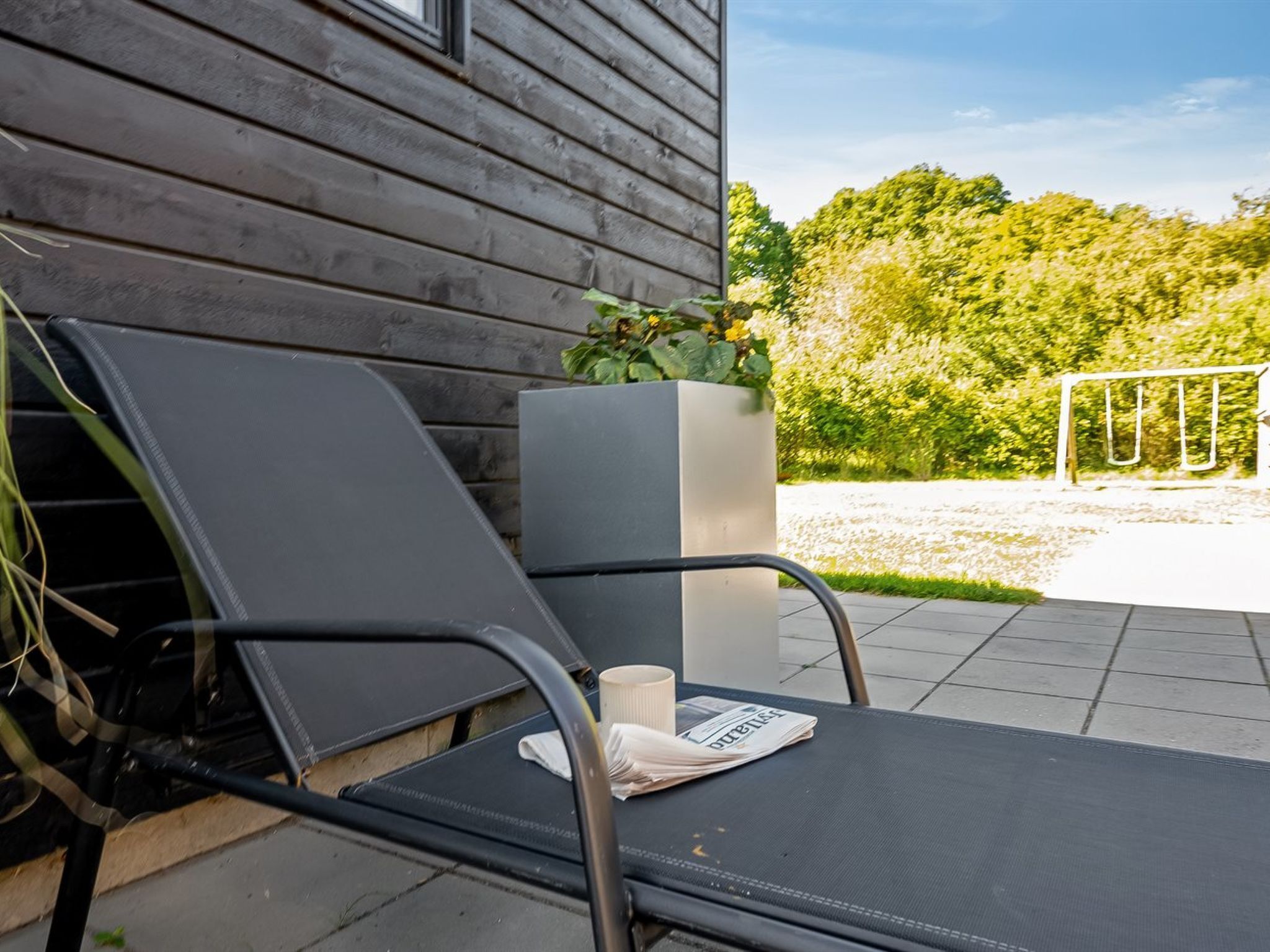 A modern outdoor seating area with a dark metal chair and a white planter with green foliage.