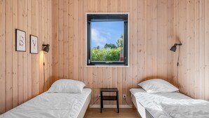 Ein Zimmer mit zwei Betten, Holzwänden, einem Fenster mit Blick auf Grünflächen und zwei Wandlampen.
