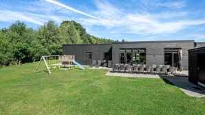 Ein modernes Gebäude mit einer Terrasse, Sitzgelegenheiten im Freien und einem Spielplatz.