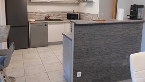 A modern kitchen with a central island, stainless steel appliances, and a stone backsplash. - Armand's House (Yssingeaux)