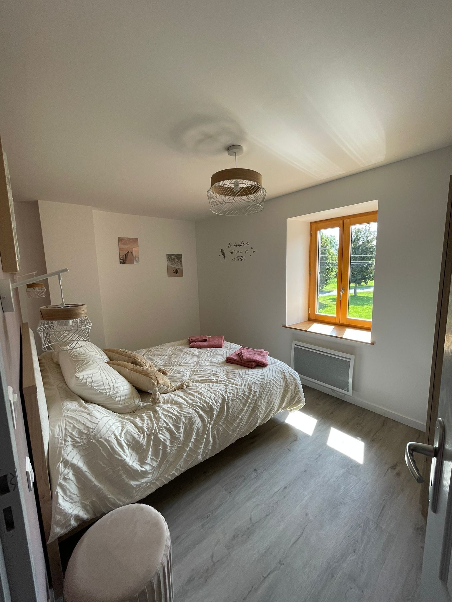 Une chambre à coucher avec un lit, une fenêtre donnant sur un espace verdoyant, un radiateur et un luminaire au plafond.