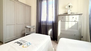 Quarto com duas camas, um guarda-roupa, uma cadeira e uma cômoda.