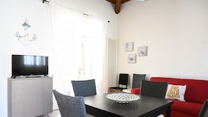 Uma sala de jantar com uma mesa, cadeiras, uma televisão sobre um móvel, um sofá vermelho e obras de arte na parede.