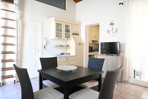 A dining area with a table, chairs, a TV, and a kitchen in the background.
