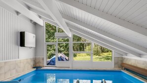 En moderne swimmingpool indendørs med skråloft, store vinduer og udsigt til det fri.