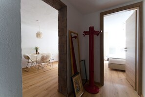 A room with a wooden floor, a dining table with chairs, a red coat rack, and a large mirror.