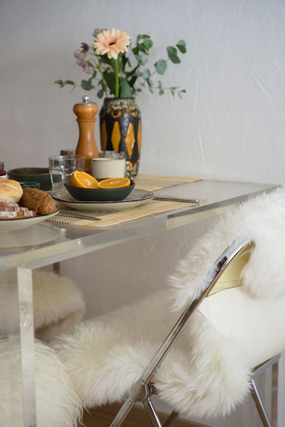 Une table à manger avec un plateau en verre, un saladier rempli de fruits, un vase avec des fleurs et un moulin à poivre décoratif.