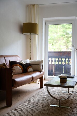 A living room with a brown leather sofa, a floor lamp, a coffee table, and a view of a balcony with a railing.