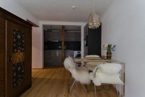 A modern kitchen with grey cabinets, a wooden floor, and a dining area with a glass table and white furry chairs. - Cosy & Style Zell am See (Zell am See)