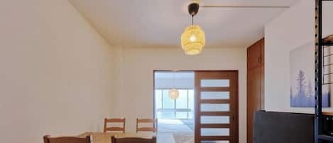 Une pièce comprenant une table à manger et des chaises, un canapé, un luminaire suspendu et une porte donnant sur une autre pièce.