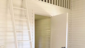 Ein heller Innenraum mit Holztür, weißer Leiter und geneigter Decke.