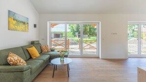 A modern living room with a green sofa, a small round table with a vase, and large glass doors leading to an outdoor area. - Vacation home "Huus Mullewap" in Kating for up to 4 people (Kating)