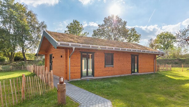 Una casa in legno con tetto spiovente, un vialetto lastricato che conduce all'ingresso e un cortile recintato.