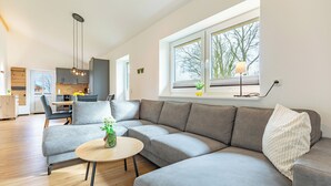 Un soggiorno moderno con un divano angolare grigio, un tavolino rotondo e, sullo sfondo, un'area da pranzo.