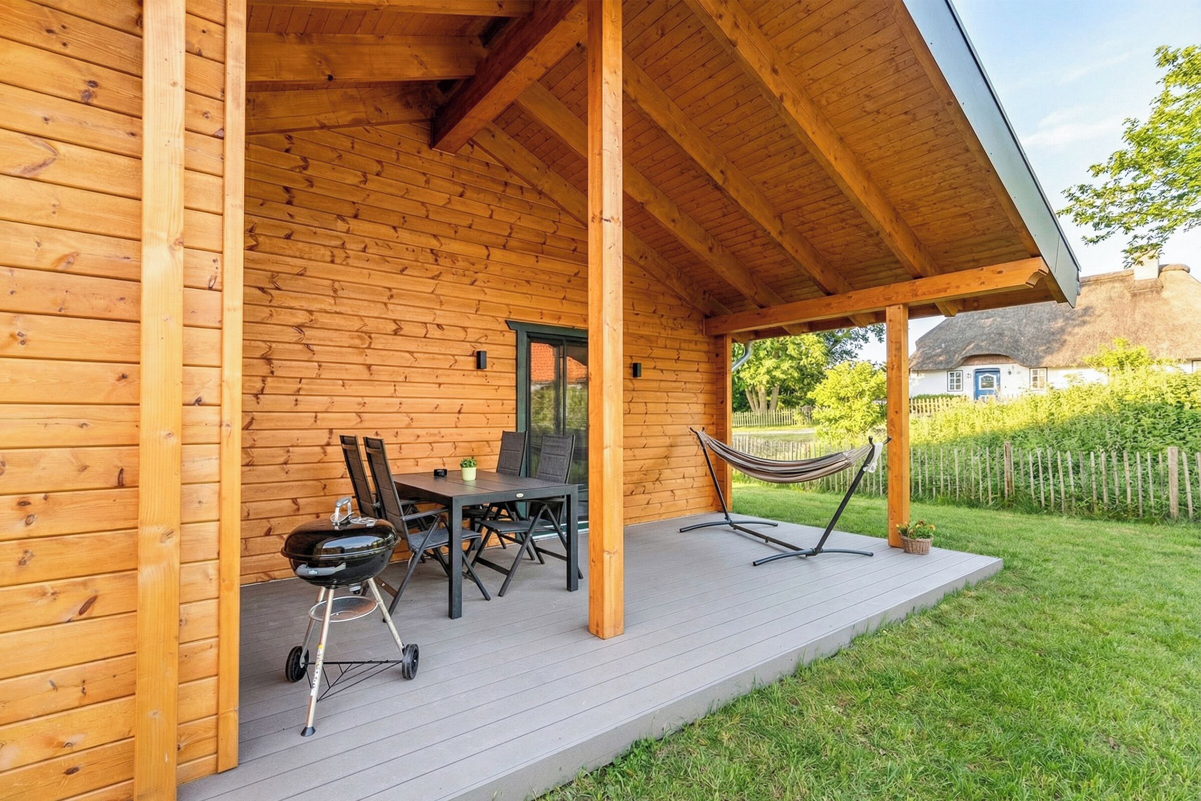 A wooden cabin with a covered porch, a table with chairs, a grill, and a hammock.