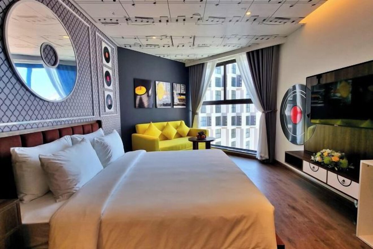 Habitación de hotel con una cama grande, un sofá amarillo, un televisor y una ventana con vistas a la ciudad.