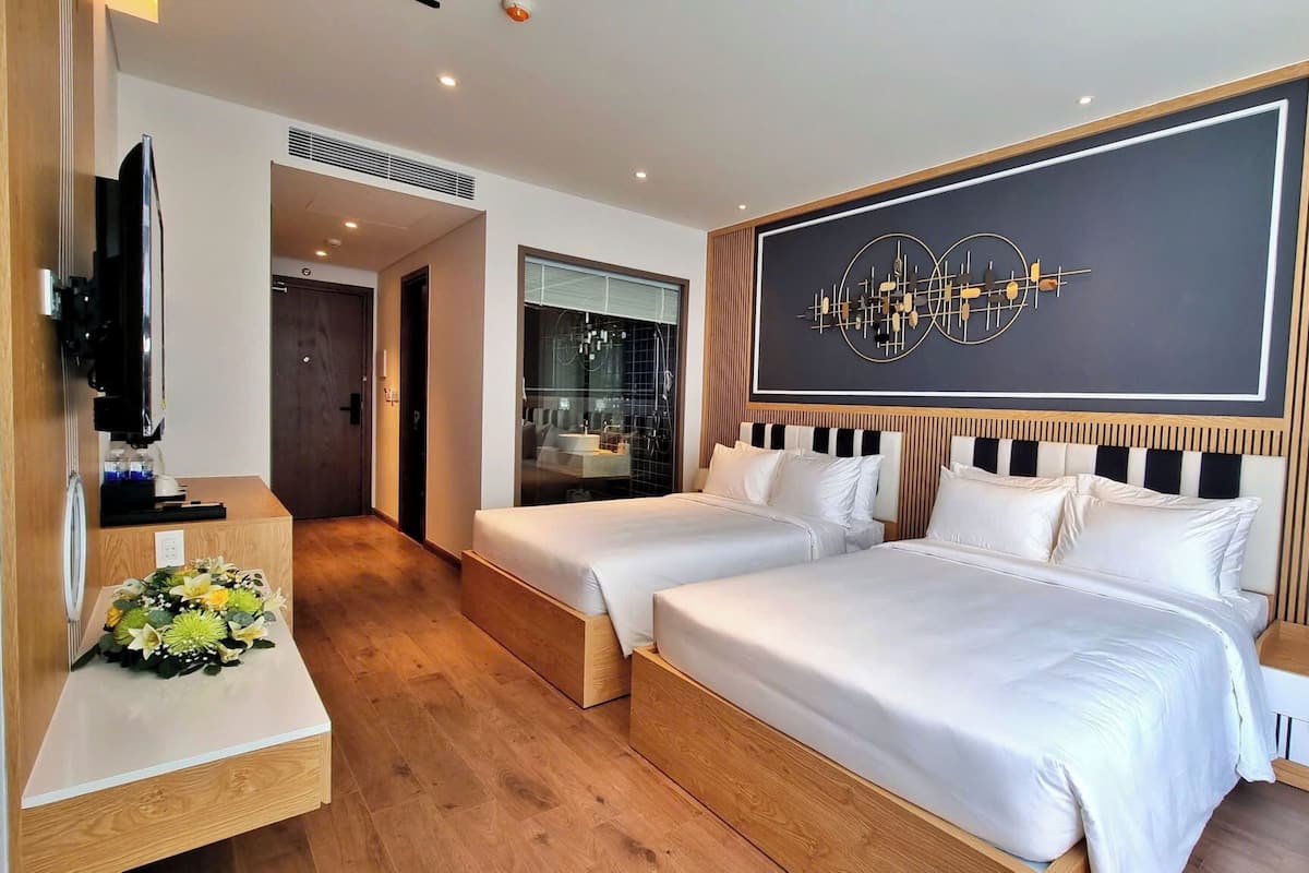 A hotel room with two beds, a TV, a desk, and a large wall clock.