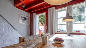 A cozy room with a wooden table, a bowl of fruit, and a newspaper. There are large windows with curtains, a staircase, and a red ceiling. - "Ulvi" - 15m from the sea by Interhome (Ebeltoft)