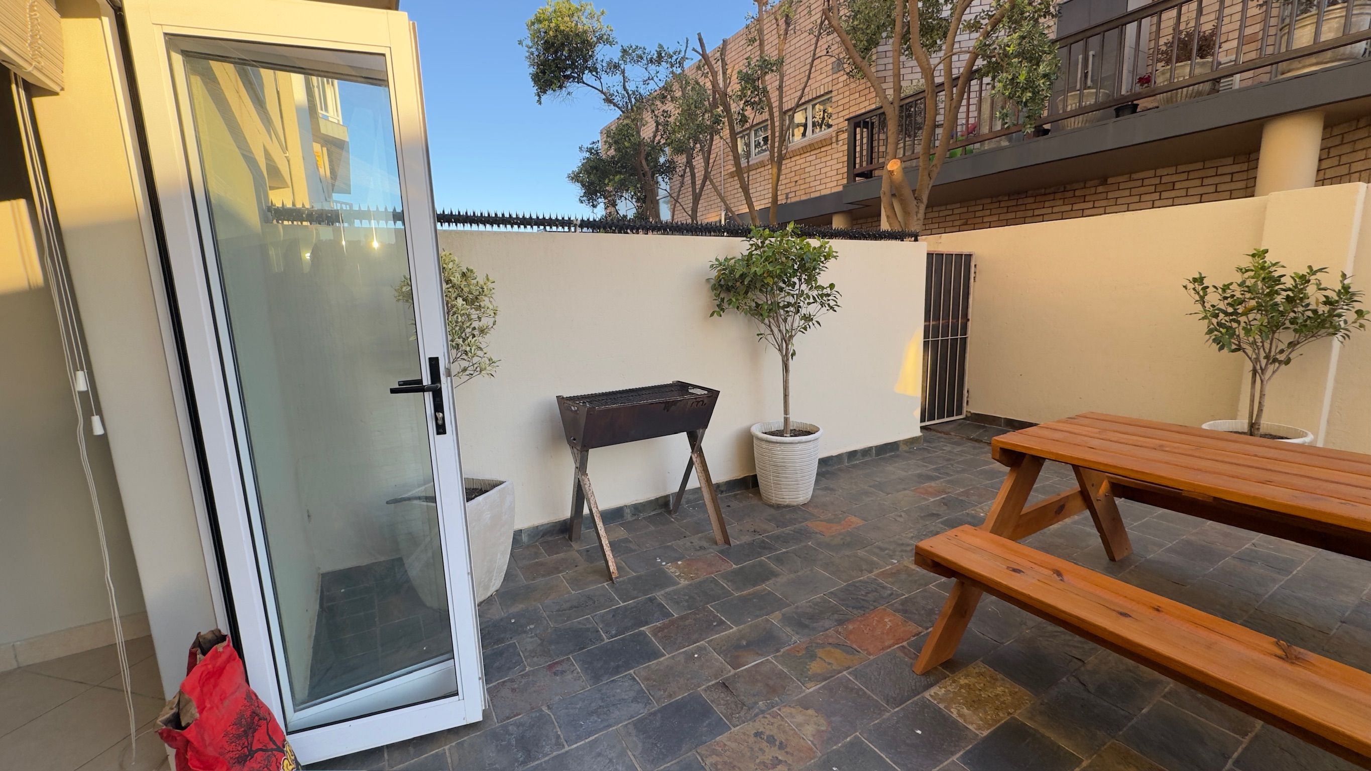 A patio area with a wooden bench, a barbecue grill, and potted plants.