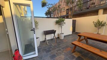 A patio area with a wooden bench, a barbecue grill, and potted plants.
