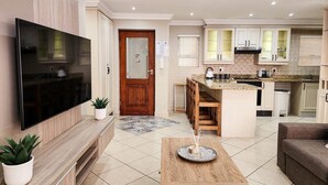 Una cocina moderna con televisor, armarios de madera y un comedor con mesa y sillas.
