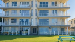Un edificio de varios pisos con balcones, ventanas amplias y un césped con una mesa de picnic.