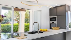 A modern kitchen with a large island, built-in appliances, and a view of greenery.