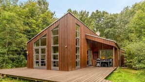 Une cabane moderne en bois, dotée d’une terrasse, de grandes fenêtres et d’une antenne parabolique.