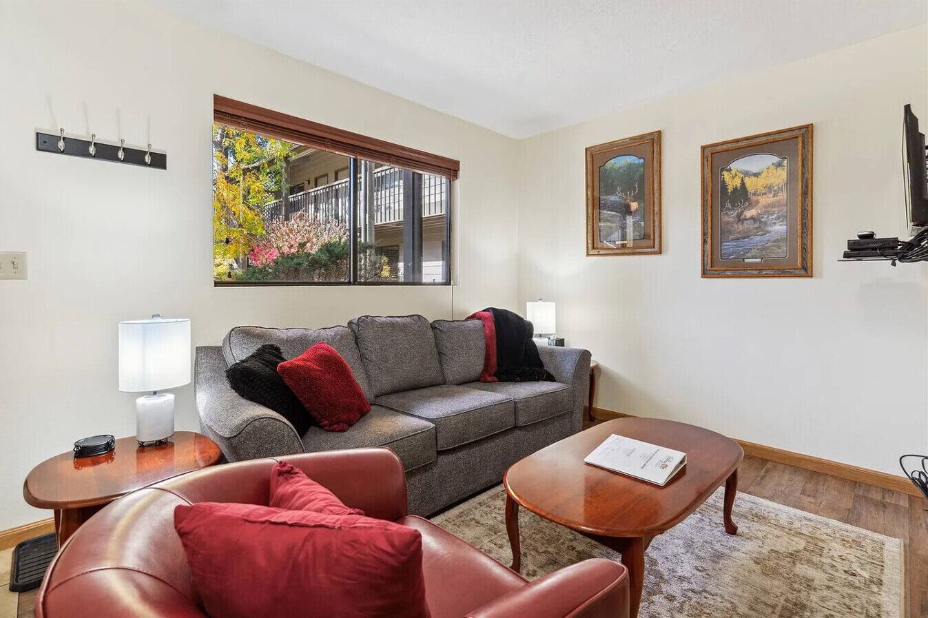 A living room with a grey sofa, red cushions, a wooden coffee table, and two wall-mounted lamps.