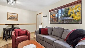 Ein Wohnzimmer mit einer Couch, einem roten Ledersessel, einem Holztisch und einem Gemälde an der Wand.