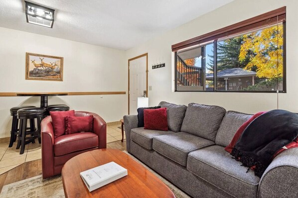 Una sala de estar con un sofá, un sillón de cuero rojo, una mesa de centro de madera y un cuadro en la pared.