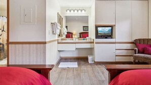 Ein kleines Hotelzimmer mit Holzboden, einem Bett mit roter Bettwäsche, einem kleinen Tisch, einem Fernseher auf einem Schrank und einem Spiegel über dem Spiegel.