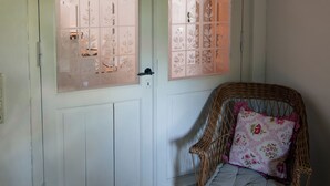 A white door with frosted glass panels, a wicker chair with a floral cushion, and a wooden ceiling.
