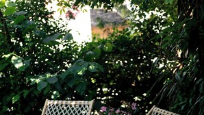 Two wicker lounge chairs with a wooden frame, positioned on a wooden deck with a garden backdrop.