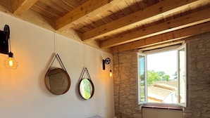 A bedroom with a wooden ceiling, a stone wall, and a large window. - Charming comfort room (Fénols)