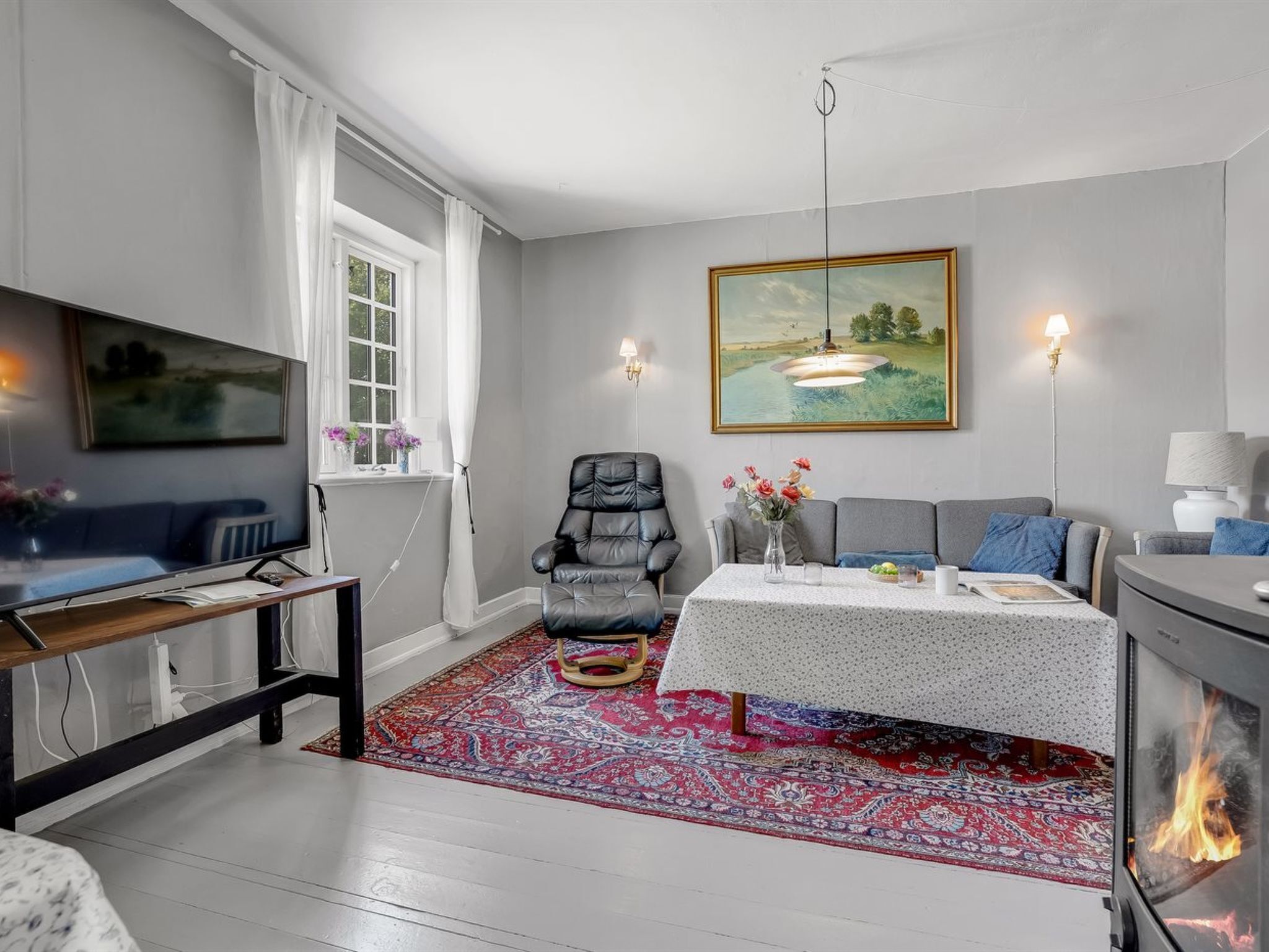 A living room with a sofa, a chair, a dining table with a rug, a fireplace, and a painting on the wall.