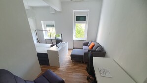 Una habitación pequeña y luminosa con piso de madera, un escritorio, una silla y un sofá.