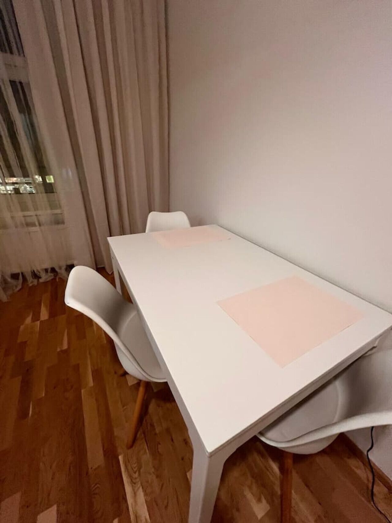 Ett konferensrum med ett vitt bord, fyra vita stolar och ett stort fönster med gardiner.