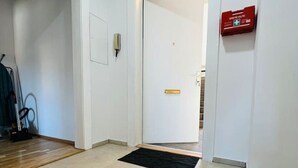 Un pasillo con un felpudo negro, una puerta blanca y una señal roja de salida de emergencia.
