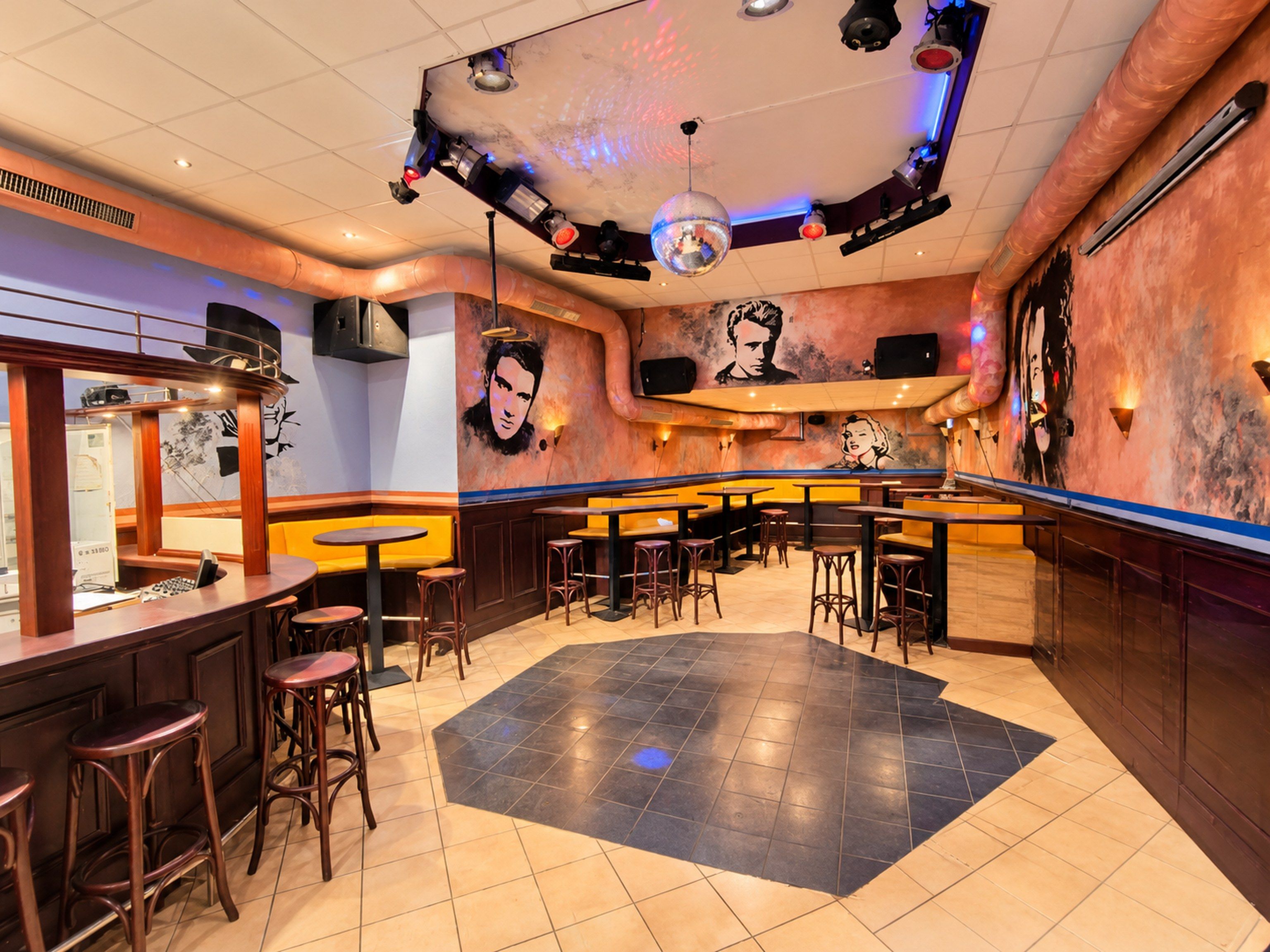 A bar area with stools, a bar counter, and a dance floor.