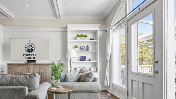 A living room with a grey sofa, a small round table, and a bookshelf. - 2BR Penthouse w/ Balcony | Grand Traverse Commons (Traverse City)